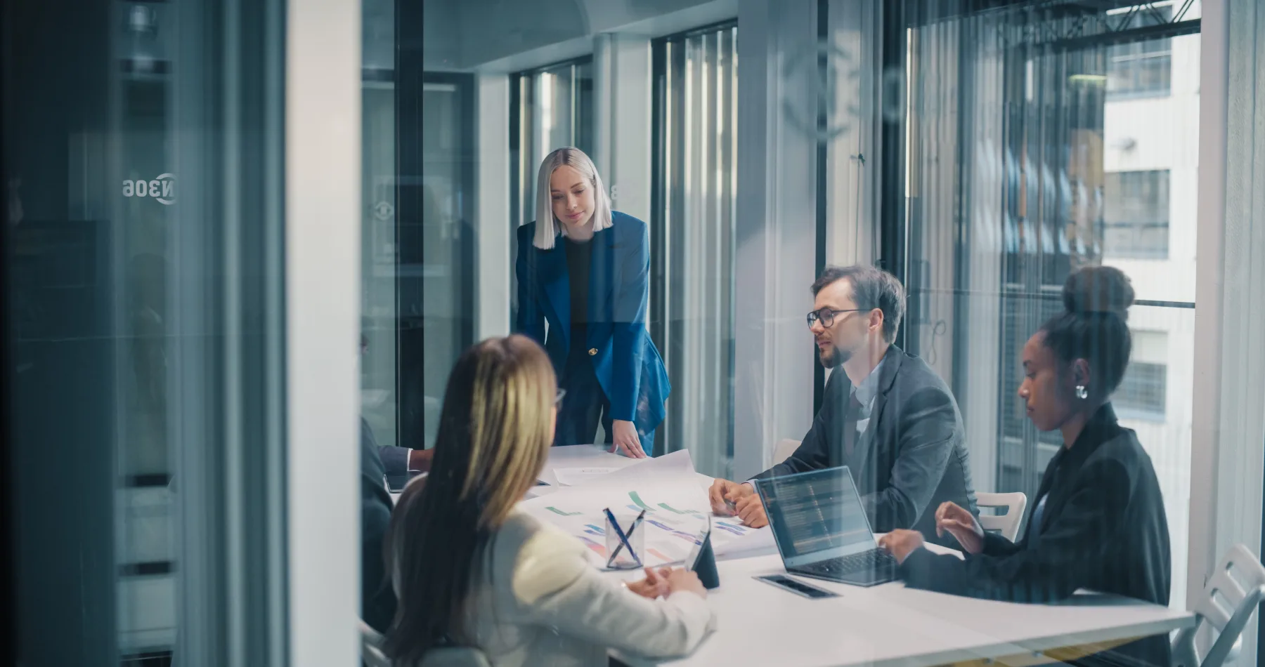 A leader running a strategy meeting with her team in a modern glass-walled office.